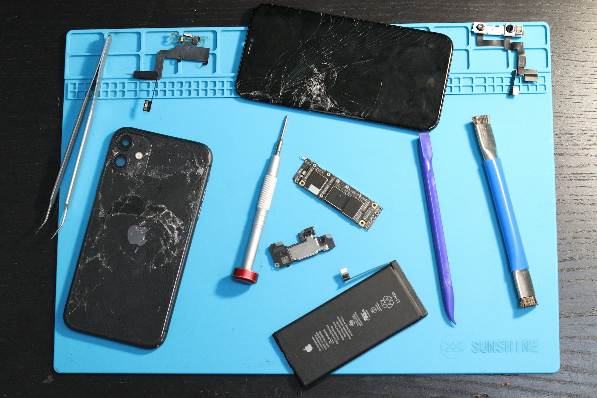 iPhone con pantalla rota, batería y herramientas de reparación